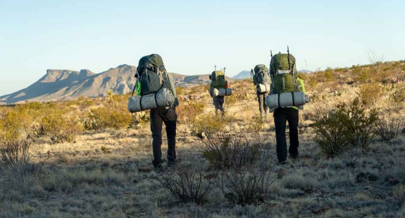 a group of gap year students carrying backpacks hike through the desert with a mountain in the background
